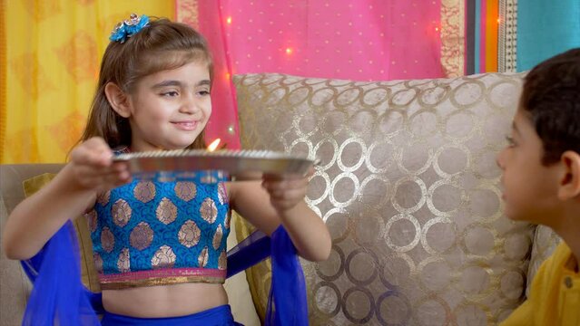 Pretty Indian girl in festive clothes performing aarti for her brother - Raksha Bandhan  Bhai Dooj  Indian festival. Young Asian siblings celebrating Rakhi/Bhaiya Dooj - traditional rituals  ethnic...