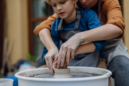 Mother teaching son how make pottery on pottery wheel. Child creative activities and art. Boy making pottery, having fun. Happy family moment.