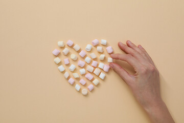 Marshmallow and hand on beige background, top view