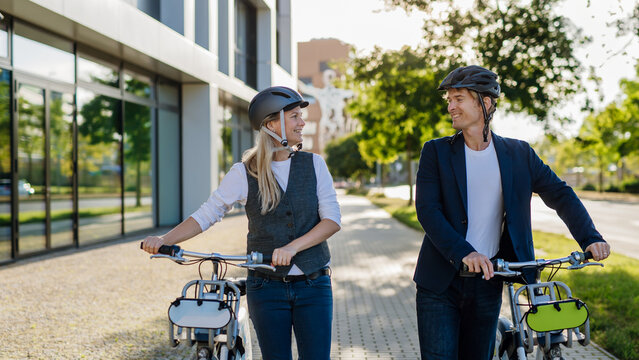 Spouses commuting through the city, talking and walking by bike on street. Middle-aged city commuters traveling from work by bike after a long workday.