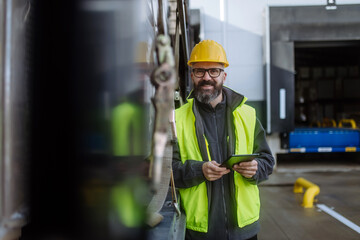 Portrait of smiling warehouse receiver standing by blue truck and holding tablet. Receiving clerk...
