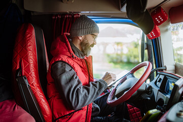 Truck driver sitting in truck, holding tablet, looking at cargo details, delivery schedule.