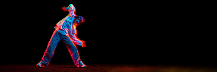 Fototapeta premium Young girl, hip hop dancer in motion, dancing isolated over black background in neon light. Concept of contemporary dance, street style, youth, hobby, lifestyle. Banner. Empty space to insert text