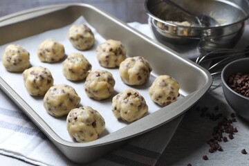 Baking pan with raw chocolate chip cookie balls on table, closeup