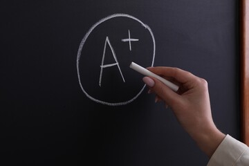 Fototapeta premium School grade. Teacher writing letter A and plus symbol with chalk on blackboard, closeup