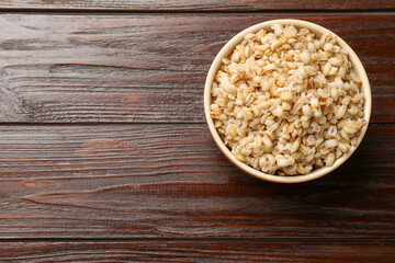 Delicious pearl barley in bowl on wooden table, top view. Space for text
