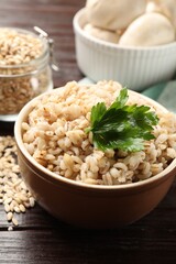 Delicious pearl barley with parsley in bowl on wooden table, closeup