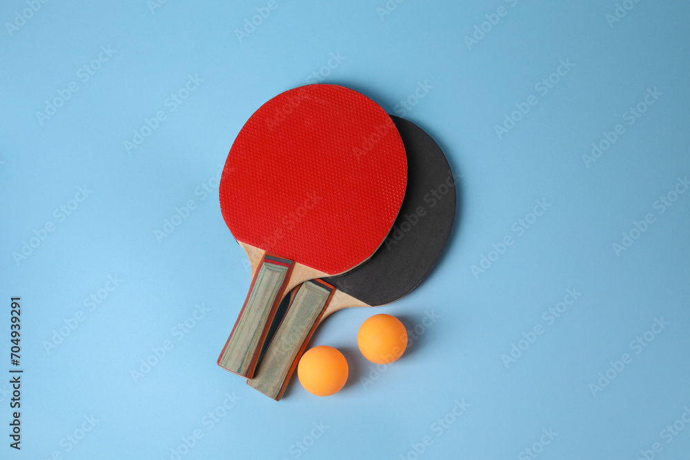 Poster Ping pong balls and rackets on light blue background, flat lay