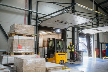 Warehouse receiver overseeing the storing of delivered items, holding tablet, looking at cargo...