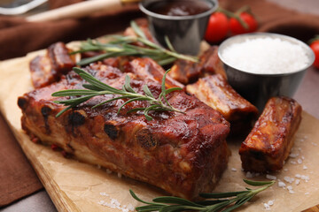 Tasty roasted pork ribs served with sauce and rosemary on brown table, closeup
