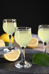 Tasty limoncello liqueur, lemon and green leaf on table, closeup
