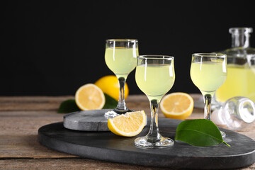 Tasty limoncello liqueur, lemons and green leaves on wooden table. Space for text