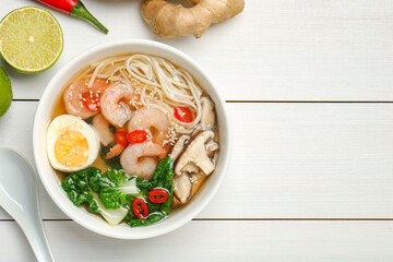 Tasty ramen with shrimps in bowl on white wooden table, flat lay. Space for text
