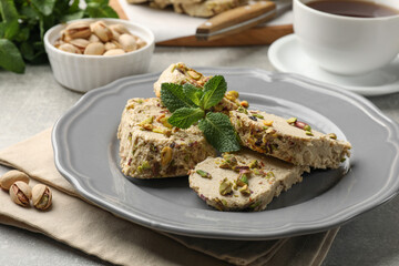 Tasty halva with pistachios and mint served on light grey table, closeup