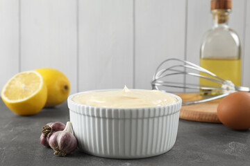 Fresh mayonnaise sauce in bowl and ingredients on grey table
