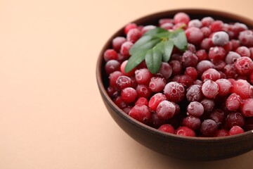 Frozen red cranberries and green leaves on beige background, closeup. Space for text