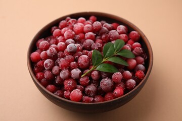 Frozen red cranberries and green leaves on beige background, closeup