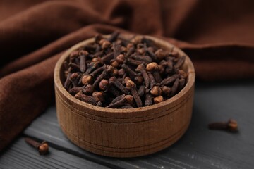 Aromatic cloves in bowl on grey wooden table, closeup