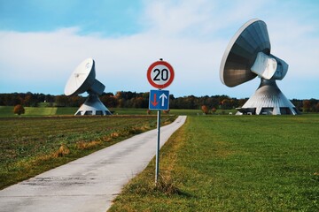 view of a small street leading between two giant satellite dishes, German road sign in the center of the picture