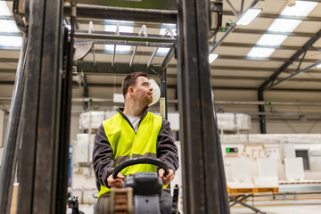 Fototapeta na wymiar Portrait of young man with Down syndrome driving forklift, working in factory, warehouse. Concept of workers with disabilities, support in workplace.