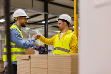 Young man with Down syndrome working in modern factory, fist bump with colleague, teamwork. Concept of workers with disabilities, support in workplace.
