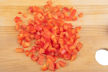 Red bell pepper cut into pieces on a wooden cutting board.