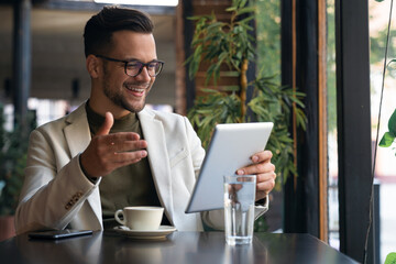 Happy young business man wearing suit sitting at Cafe using digital tablet. Confident businessman...