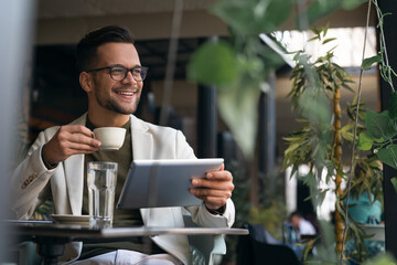 Happy smiling relaxed man, young professional businessman entrepreneur sitting in outdoor Cafe...