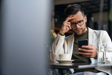 Serious focused businessman sitting in a Cafe using smartphone for texting, surfing the net, using...