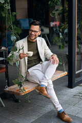 Happy smiling relaxed man, young professional businessman entrepreneur sitting on a swing in modern...