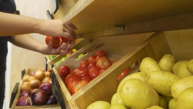 putting tomatoes on shelf. Close up of unrecognizable african american woman adding fresh products in grocery store. 