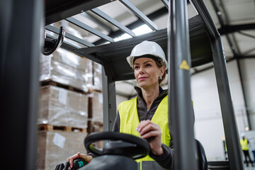 Female warehouse worker driving forklift. Warehouse worker preparing products for shipmennt,...
