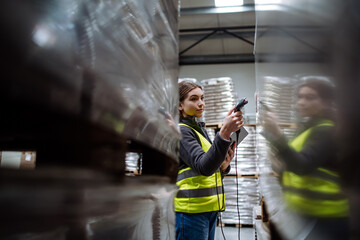 Female warehouse worker holding scanner, scanning the barcodes on products in warehouse. Warehouse manager using warehouse scanning system. - obrazy, fototapety, plakaty