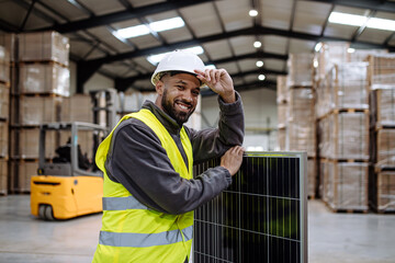Handsome worker holding solar panel in warehouse, factory. Solar panel manufacturer, solar...