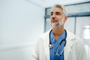 Portrait of confident mature doctor standing in Hospital corridor. Handsome doctor with gray hair...