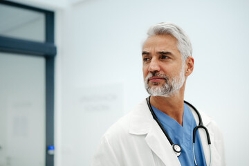 Portrait of confident mature doctor standing in Hospital corridor. Handsome doctor with gray hair...