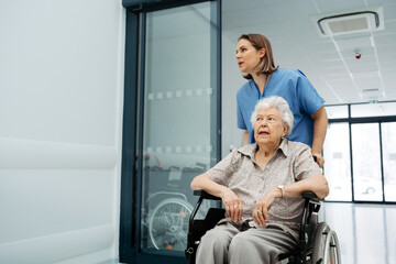Portrait of nurse pushing senior patient in wheelchair across hospital corridor. Emotional support...