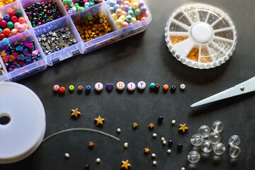 Colorful beads and various jewelry making supplies on dark background. Letter beads spelling I heart DIY. Selective focus.