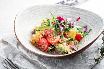 Fresh salad with quinoa, avocado, tomatoes and vegetables in a gray ceramic bowl on a concrete background. Dietary healthy dish for vegans, selective focus