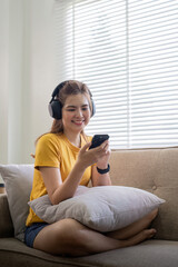 Obraz premium Young asian woman using mobile phone and earphones to listening to music or online chatting at home
