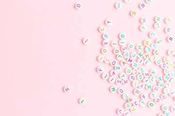 Beads with letters scattered on a pink background. Place for text.