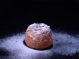 Shu cake in powdered sugar, on black glass, copy space