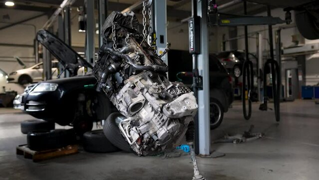 A car engine hangs on chains at a service station. Internal combustion engine repair