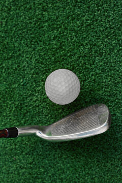 Vertical photo of a golf club and a ball on green artificial grass. Training before the start of the competition.