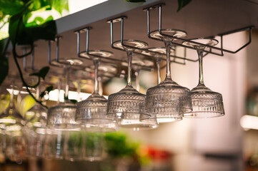 Many glasses hanging from bar rack closeup. Glasses hang over bar counter. The glasses are turned...