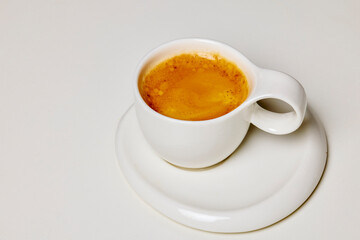a white cup with coffee on a plate.
