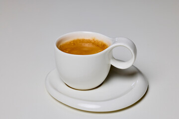 a white cup with coffee on a plate.