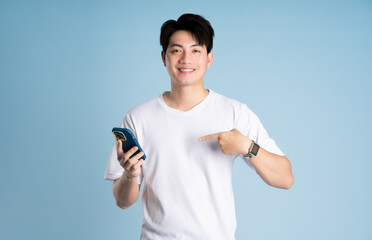 Fototapeta premium Portrait of Asian guy using phone and posing on blue background