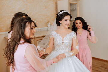 A friend helps the bride fasten her dress. A woman helps her friend fasten the buttons on the back of her wedding dress. The morning of the bride, the creation of a family, an important event.