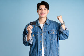 Portrait of an Asian guy wearing a jacket and holding card credit posing on a blue background